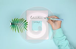 Female hand holding a pen and writing `education` in notepad.