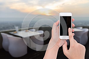 Female hand holding a phone on blurry dinner table set with sun