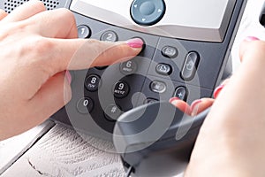 Female hand holding phone receiver and dialing number