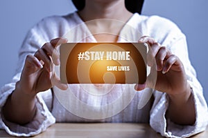 Female hand holding phone with text `STAY HOME SAVE LIVES` viral social media message sign, social distancing, COVID-19 Coronavi