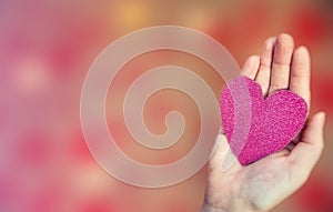 Female hand holding pink glitter heart on romantic blurred bokeh background, copy space or space for text, Valentine`s