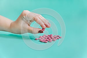 Female hand holding  pink pills. Turquoise background. Close-up view