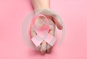 Female hand holding pink ribbon on color background. Breast cancer awareness concept
