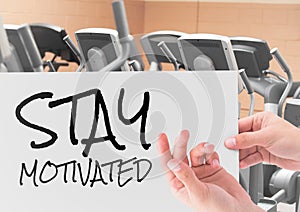 Female hand holding placard with text stay motivated in gym