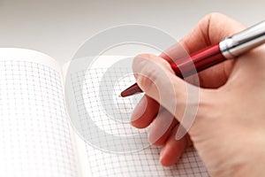 Female hand holding a red ballpoint pen on the empty notebook