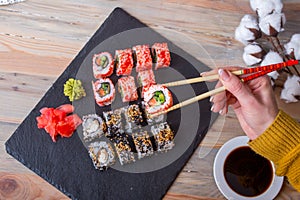 Female hand holding a roll of chopsticks over sushi roll