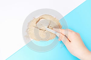 Female hand holding scoop with protein powder on blue and pink background top view.