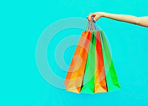 Female hand holding and showing colorful shopping bags on blue background