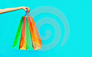 Female hand holding and showing colorful shopping bags on blue background