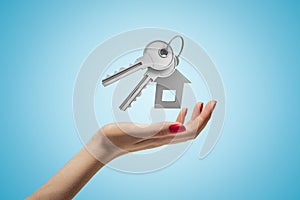 Female hand holding silver key and a house shape key fob on blue background