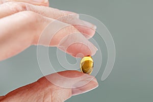 Female hand holding a small yellow capsule of nutritional supplement. Food supplement, vitamin D, omega, vitamin C.