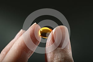 Female hand holding a small yellow capsule of nutritional supplement. Food supplement, vitamin D, omega, vitamin C.