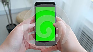 Female hand holding smartphone with green screen at home