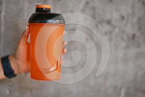 Female hand holding sports bottle with water against grey wall at gym, selective focus