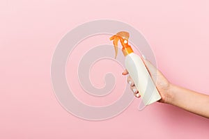 Female hand holding spray cream bottle of lotion . Girl give cosmetic products on pink background