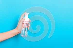 Female hand holding spray cream bottle of lotion isolated. Girl give cosmetic products on blue background
