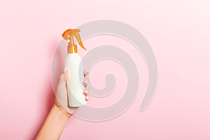 Female hand holding spray cream bottle of lotion isolated. Girl give cosmetic products on pink background