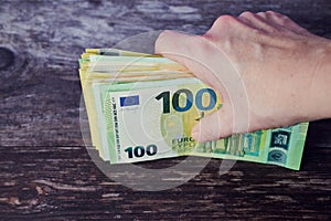 Female hand is holding a stack of Euro banknotes against wooden surface