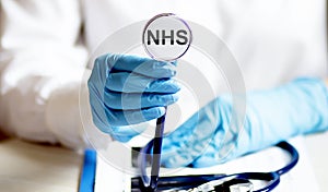 Female hand holding stethoscope with text NHS health care concept photo