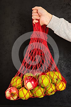 Female hand holding a string bag with fruits on black background. Eco friendly mesh bag - alternative to plastic bags
