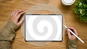 A female hand holding a stylus pen using tablet, tablet white screen mockup is on a wooden tabletop