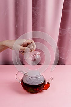 Female hand holding tea pot lid above kettle with the steaming fruit and berry tea,