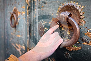 Female hand holding on to the ring of an old medieval door