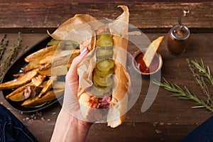 Female hand holding traditional American hot dog on the wooden board. Top view.