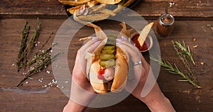 Female hand holding traditional American hot dog on the wooden board. Top view.