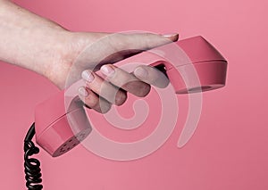 Female hand holding vintage corded phone handset on pink background. Retro concept