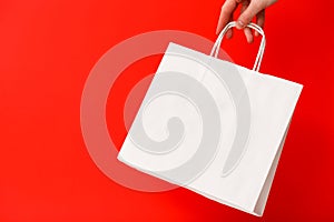 Female hand holding white blank shopping bag isolated on red background. Black friday sale, discount, recycling