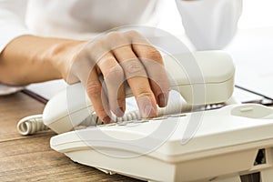 Female hand holding a white landline telephone handset and dialing a phone number