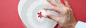 Female hand holding white piece of puzzle in shape of heart close-up