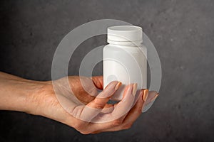 Female hand holding a white plastic bottle with pills. Capsules, collagen, vitamins, pain killers or drugs