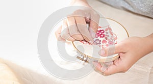 Female hand holding wood embroidery frame and and needle working on flower pattern stitching in a process of handiwork