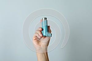 Female hand holds asthma inhaler on light gray background