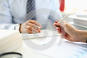 Female hand holds ballpoint pen over documents closeup in front of man in background in office