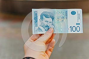 Female hand holds a banknote of 100 one hundred Serbian dinars on a street in the city