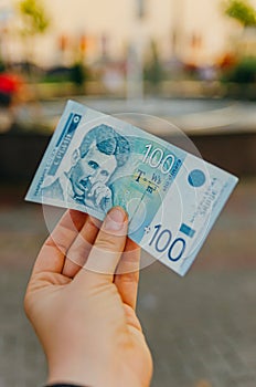 Female hand holds a banknote of 100 one hundred Serbian dinars on a street in the city