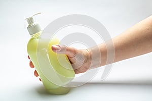 Female hand holds a bottle with liquid yellow soap on a white background. Horizontal orientation