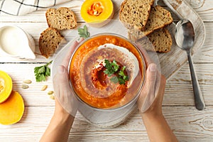 Female hand holds bowl of pumpkin soup on white wooden