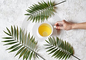 A female hand holds a cup of green natural tea on a white concrete background. Rest in warm tropical countries concept