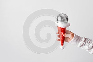 Female hand holds disco ball ice cream and santa hat waffle cone on white background. Merry Christmas concept