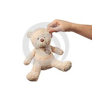 Female hand holds the ear of a small beige cute teddy bear with patches