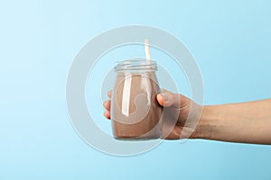 Female hand holds glass chocolate milkshake on blue background