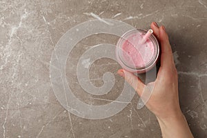 Female hand holds glass strawberry milkshake on gray background