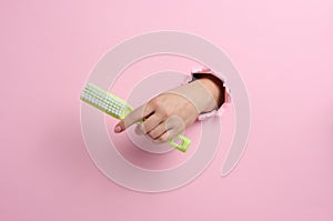 Female hand holds a green plastic brush on a pink background. A part of the body sticks out of a hole with torn edges in a paper