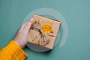 female hand holds a handmade gift in craft paper, yellow maple leaf, autumn discounts concept
