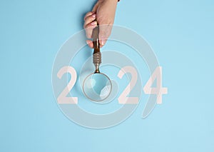 A female hand holds a magnifying glass and the inscription 2024