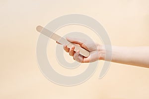 A female hand holds a nail file on a beige  background. The concept of beauty and self-care. Image for your design